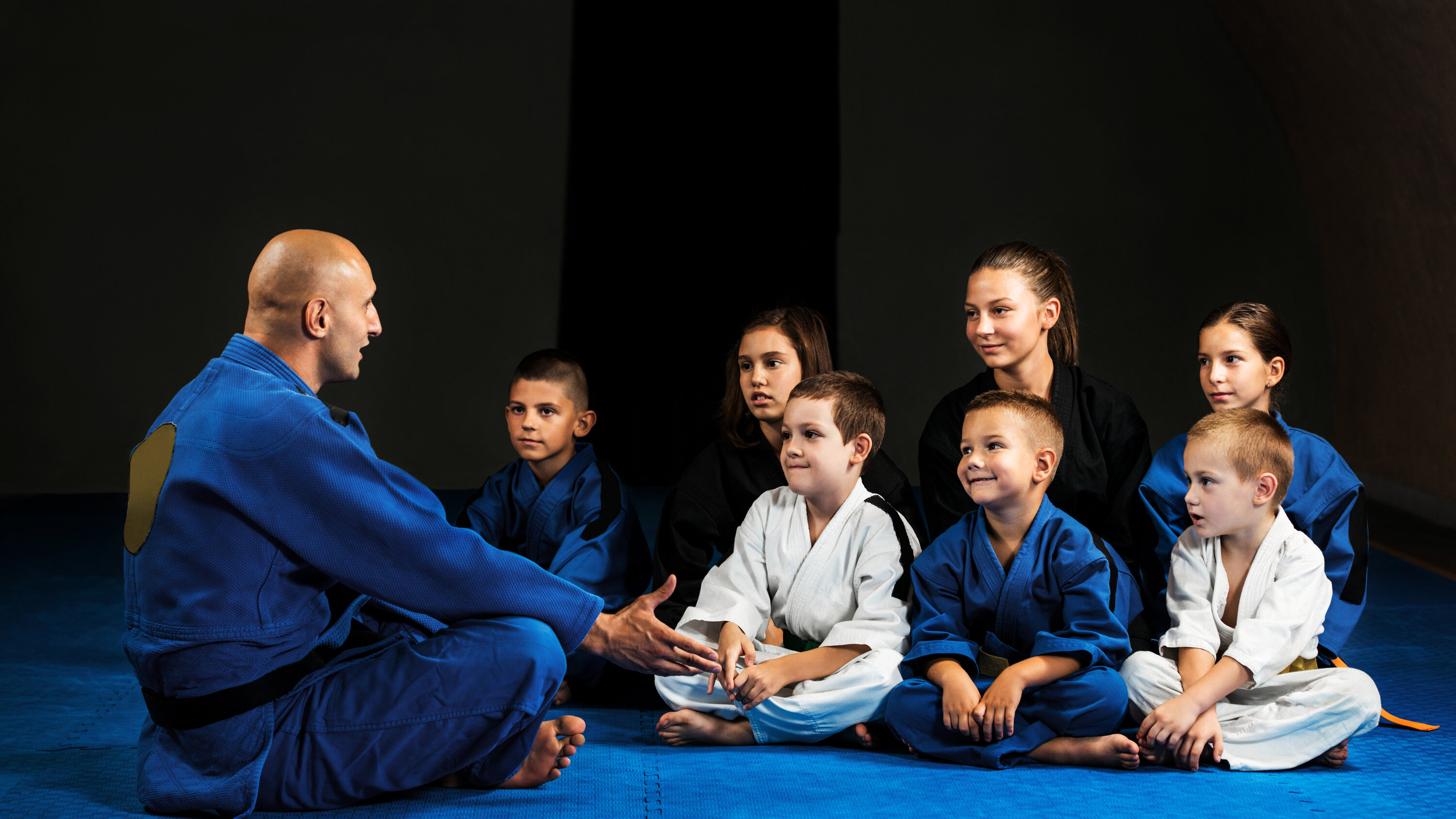Kinder sitzen mit Trainer auf der Matte